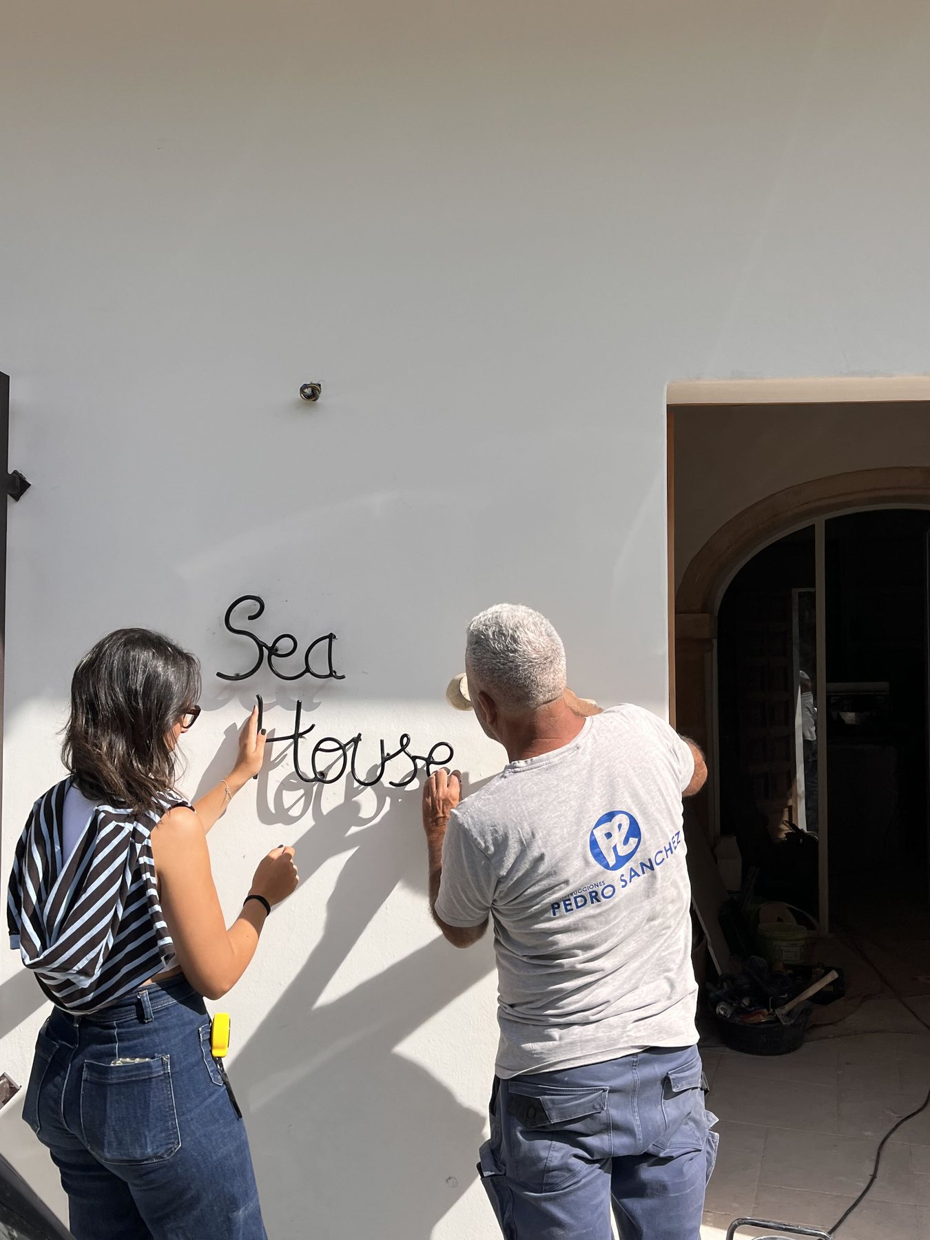 The Sea House sign, in black wrought iron, being fixed to the white façade.